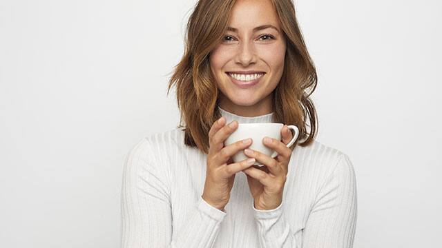 Γυναίκα που χαμογελά και κρατά το φλιτζάνι του καφέ